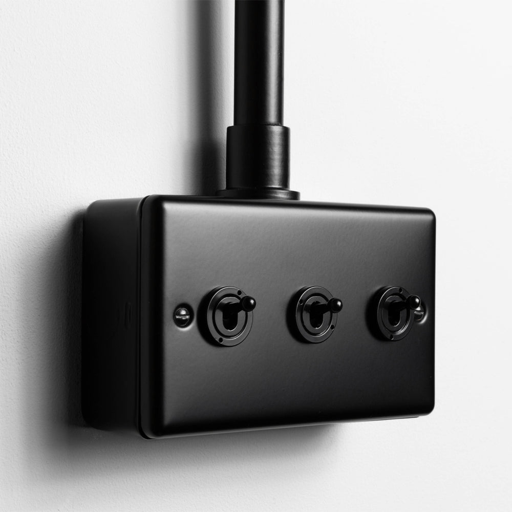 Matt Black 3 Gang 2 Way Toggle Switch With Back Box And Conduit On Light Grey Background